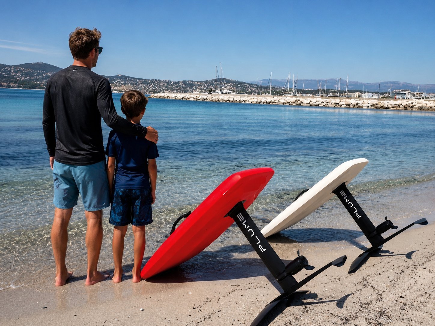 Père et fils face à la mer avec deux planches eFoil Plume rouge et blanche